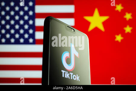 TikTok app Logo auf einem Bildschirm des Smartphones und Fahnen von China und USA auf die verschwommenen Hintergrund. Die App ist in der Mitte der Spannungen zwischen den USA und China. Stockfoto