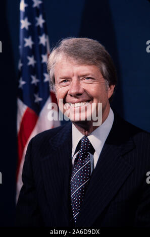 Porträt von Präsident Jimmy Carter in dunklem Anzug mit US-Flagge im Hintergrund. (1977) Stockfoto