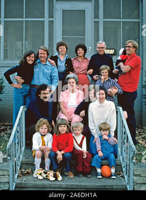 16 Mitglieder einer amerikanischen Familie darstellen, im Freien in 1975 auf den Stufen vor der Familie zu Hause. Die ältere grauhaarige Paar zeigen ihre zwei Söhne und zwei Töchter mit ihren Ehefrauen und Ehemänner und sechs Enkelkinder (darunter ein schlafendes Baby in der hintersten Reihe versteckt). Anlass war die jährliche Zusammenkunft der Familie in der Weihnachtszeit. Die 70er Jahre Frisuren und Kleidung. Stockfoto