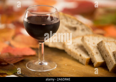 Herbst Aromen und Farben: ein Glas Rotwein mit Scheiben Vollkornbrot im Hintergrund auf einem alten hölzernen Schneidebrett mit Rot und Orange wis Stockfoto