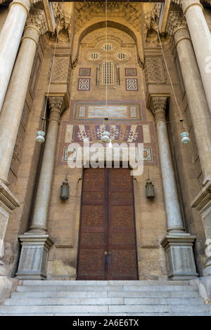 Seite Eingang von Al Rifai Moschee, der alten Steine Steinwand mit Arabesque eingerichteten hölzernen Tür umrahmt von Marmor graviert zylindrische Lichtmasten, mittelalterliche Kairo Ägypten Stockfoto