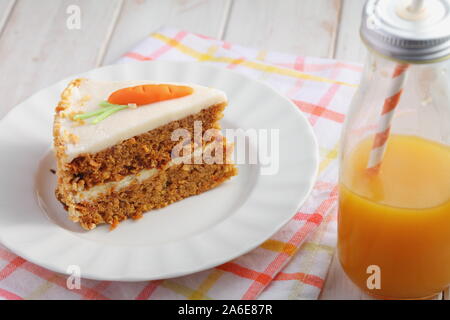 Stück Karottenkuchen Pastel de zanahoria mit Zuckerguss und Marzipan Karotten auf weißem Hintergrund mit Karottensaft. Pastellfarben Stockfoto