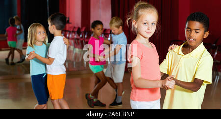 Gruppe von froh lächelnde Fröhliche positive Kinder versucht, Tanzen mit Partner im Klassenzimmer Stockfoto