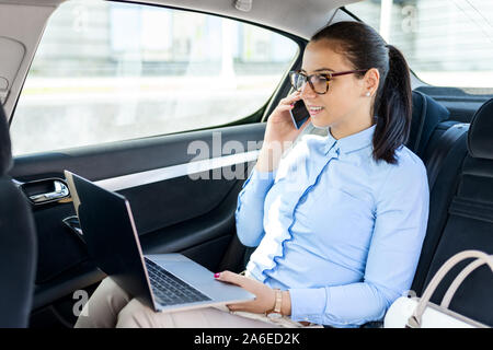 Business Frau im Auto sitzt und spricht auf der Zelle. In einem Auto auf dem Telefon Geschäftsfrau. Schöne Geschäftsfrau im Auto. Geschäfts- und lifes Stockfoto