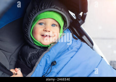 Portrait von niedlichen kaukasischen Toddler boy in Schwarz mit Kapuze warme isolierte Dawn insgesamt Jacke und blaue Decke im Kinderwagen sitzen und genießen Sie die Spaziergänge Stockfoto