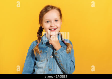 Nahaufnahme eines Kindes in einer jeanshemd auf gelbem Hintergrund. Kleines Mädchen lächelt und sieht in die Kamera. Stockfoto