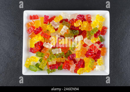 Bunte Jelly candy auf eine weisse Platte auf schwarzem Hintergrund, Ansicht von oben Stockfoto