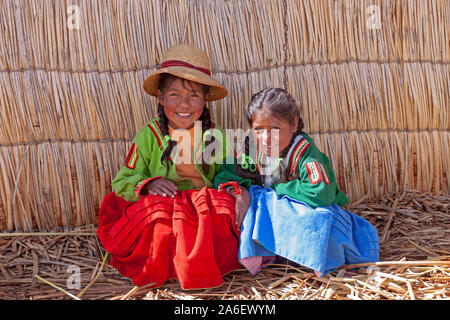 Ein Porträt von zwei jungen Mädchen vor eine Strohhütte sitzen auf einem schwimmenden Uro Insel im Titicacasee, Puno, Peru. Stockfoto