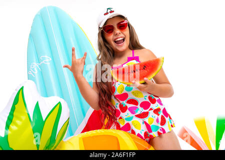 Coole Mädchen mit langen gekreuzigt Haar in Sonnenbrille und Sonnencreme, steht in der Nähe von aufblasbaren Matratzen mit einer Wassermelone Stockfoto