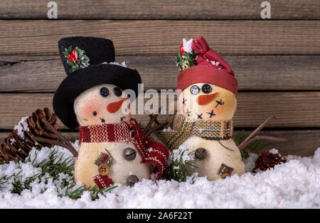 Zwei urlaub Schneemänner Figürchen auf Schnee gegen einen rustikalen Holzmöbeln Hintergrund Stockfoto