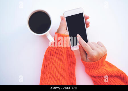 Mockup Bild der Frau Hände halten weiß Handy mit leeren schwarzen Bildschirm beim Trinken von Kaffee auf isoliert weißer Hintergrund Stockfoto