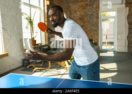 Junger Mann Tischtennis spielen am Arbeitsplatz, Spaß zu haben. Modell legere Kleidung spielen Ping pong zusammen an einem sonnigen Tag. Konzept der Freizeitgestaltung, Sport, Freundschaft, Teambuilding, Teamarbeit. Stockfoto