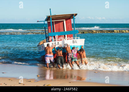 Fünf Männer drücken ein Fischerboot in den Ozean in Arembepe, Bahia - Brasilien Stockfoto