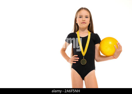 Bild einer Turnerin Mädchen in weißen kurzen Socken und schwarze Trico volle Höhe steht mit gelben Ball in die Hände und eine Medaille um den Hals isoliert Stockfoto