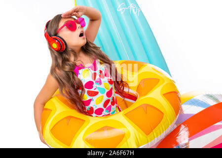 Coole Mädchen mit langen gekreuzigt Haar in Sonnenbrille und Sonnencreme, steht in der Nähe von aufblasbaren Matratzen in einem Ring aus Gummi und sieht zur Seite Stockfoto