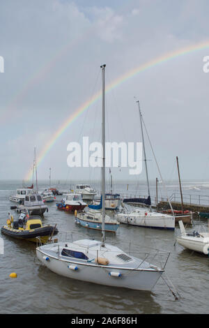 Regenbogen über dem Meer, Boote, Hafen und Strand in Lynmouth bei stürmischem Wetter, Devon, UK, September. Höhe Tide, Stockfoto