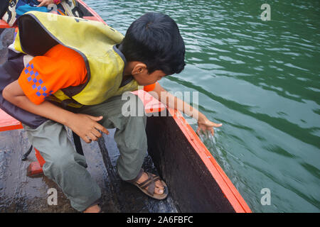 Ein junger Mann, Rettungsweste sitzen auf einem hölzernen Boot Gefühl das Wasser wie es segelt in Dawki Fluss os Shillong in Meghalaya. Stockfoto