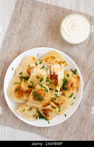 Hausgemachte, traditionelle polnische gebraten Kartoffel pierogis auf eine weiße Platte mit saurer Sahne, Ansicht von oben. Overhead, von oben, flach. Stockfoto