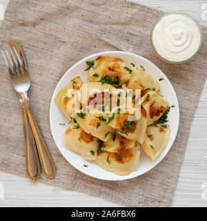 Hausgemachte, traditionelle polnische gebraten Kartoffel pierogis auf eine weiße Platte mit saurer Sahne, Ansicht von oben. Overhead, von oben, flach. Close-up. Stockfoto