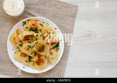 Hausgemachte, traditionelle polnische gebraten Kartoffel pierogis auf eine weiße Platte mit saurer Sahne, Ansicht von oben. Von oben, flach und Overhead. Kopieren Sie Platz. Stockfoto