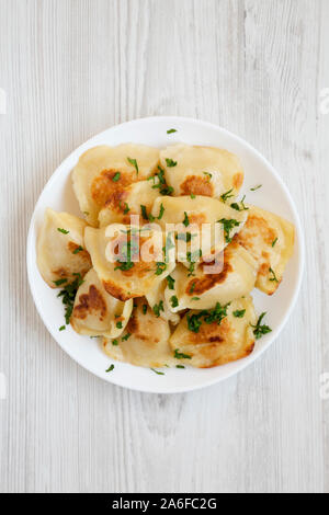 Hausgemachte, traditionelle polnische gebraten Kartoffel pierogis auf einem weißen Teller auf einem weißen Holz- Oberfläche, Ansicht von oben. Von oben, flach und Overhead. Stockfoto