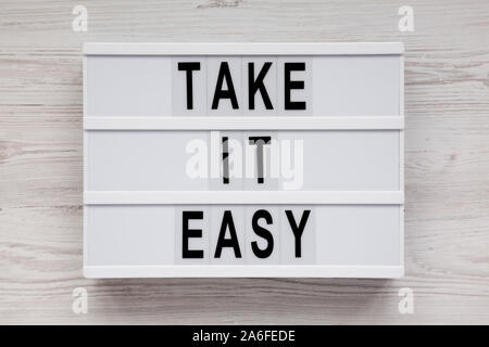 'Take it easy' Worten auf einem Leuchtkasten auf einem weißen Holz- Oberfläche, Ansicht von oben. Overhead, von oben, flach. Stockfoto