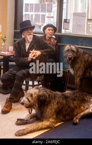 Paar in traditionellen Goth Kostüme mit Irish Wolfhound Hunde in Cafe, Whitby Goth Wochenende Festival, Whitby, North Yorkshire, UK, 26. Oktober 2019 Stockfoto