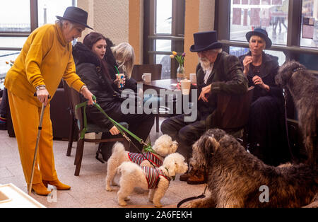 Paar in traditionellen Goth Kostüme mit Irish Wolfhound Hunde treffen Frau in gelber Kleidung mit zwei kleinen weißen Hunde, Whitby Goth Wochenende Festival, Whitby, North Yorkshire, UK, 26. Oktober 2019 Stockfoto