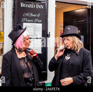 Zwei Frauen in traditionellen Goth Kostüme vaping außerhalb Pub, Whitby Goth Wochenende Festival, Whitby, North Yorkshire, UK, 26. Oktober 2019 Stockfoto