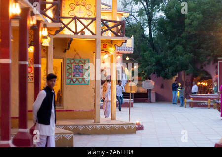 Mann, der eine weiße kurta Pyjama und Weste stehen Leute auf der Außenseite von einem reich verzierten haveli Palast in Rajasthan, Hilfe Stockfoto