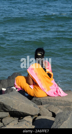 PONDICHERRY/INDIEN - 23. FEBRUAR 2018: Indische Frau im Sari sitzt auf einem Felsen und blickt auf das Meer. Stockfoto