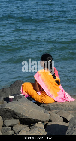 PONDICHERRY/INDIEN - 23. FEBRUAR 2018: LAND Baden-württemberg/INDIEN - 23. FEBRUAR 2018: Indische Frau im Sari sitzt auf einem Felsen und blickt auf das Meer. Stockfoto