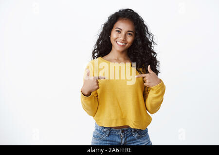 Business und Erfolg Konzept. Attraktive lächelnd Afrikanisch-amerikanische Frau im gelben Pullover, sich Stolz zeigen, großspurig, prahlende eigene Stockfoto