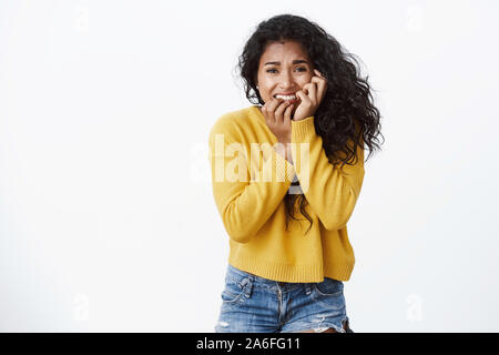 Angst, Angst, junge afrikanische amerikanische Frau im gelben Pullover, beißen Finger, runzelte die Stirn und Gesicht berühren, aus Furcht, Angst, starren Kamera stoppen Stockfoto