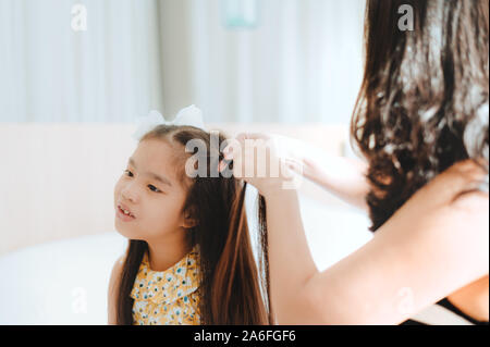 Asiatische Mutter kämmen Tochter im Bett Stockfoto