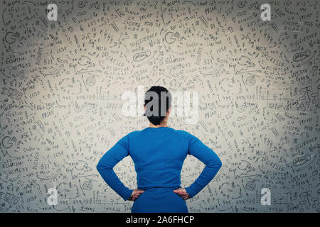 Rückansicht eines verwirrten Frau vor einer Wand, die Hände auf den Hüften, versuchen Mathematik Berechnung, Formeln und Gleichungen zu lösen. Das Denken des Projekts Stockfoto