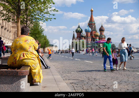 Russland Moskau 2019-06-17 Rückansicht der dicken Frau im gelben Kleid sitzt auf der Bank, in der St. Basil's Kathedrale. Menschen gehen auf dem Roten Platz. Konzept Stockfoto