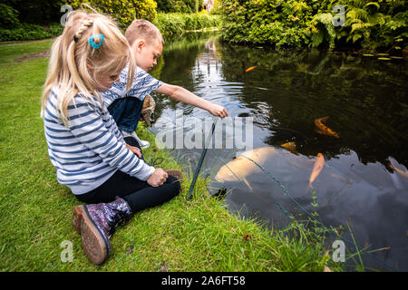 Ein schöner kleiner Junge mit ADHS, Autismus, Asperger-syndrom feeds Fisch mit seinen hübschen kleinen Schwester von einem großen Teich, See Stockfoto