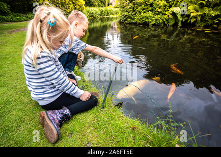 Ein schöner kleiner Junge mit ADHS, Autismus, Asperger-syndrom feeds Fisch mit seinen hübschen kleinen Schwester von einem großen Teich, See Stockfoto