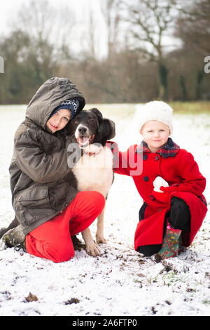 Ein schöner kleiner Junge mit ADHS, Autismus, Asperger-syndrom stellt mit seiner Schwester und seinem treuen Hund in die verschneiten Felder zu Weihnachten, Xmas Stockfoto