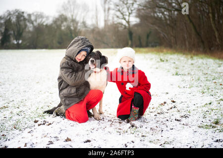 Ein schöner kleiner Junge mit ADHS, Autismus, Asperger-syndrom stellt mit seiner Schwester und seinem treuen Hund in die verschneiten Felder zu Weihnachten, Xmas Stockfoto