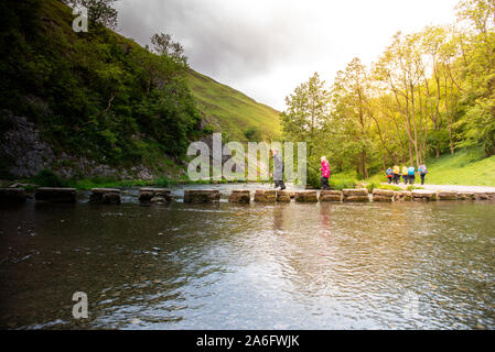 Einen kleinen Jungen und Mädchen hoffen, über die dovedale Trittsteine über einen Fluss, Bach im Peak District National Park, Derbyshire, Autismus springen Stockfoto