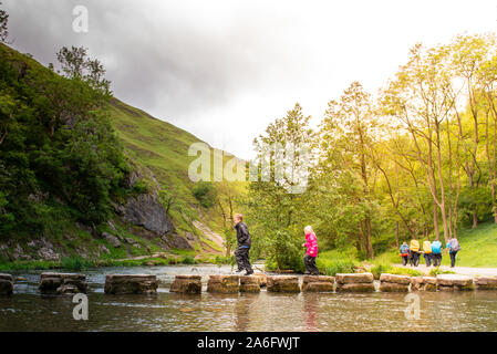 Einen kleinen Jungen und Mädchen hoffen, über die dovedale Trittsteine über einen Fluss, Bach im Peak District National Park, Derbyshire, Autismus springen Stockfoto