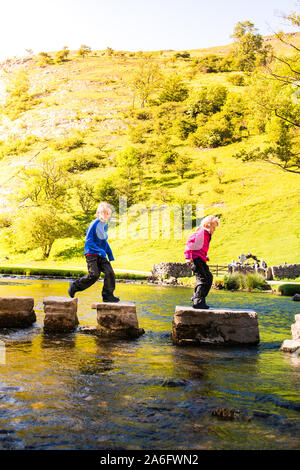 Einen kleinen Jungen und Mädchen hoffen, über die dovedale Trittsteine über einen Fluss, Bach im Peak District National Park, Derbyshire, Autismus springen Stockfoto