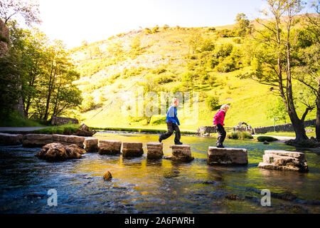 Einen kleinen Jungen und Mädchen hoffen, über die dovedale Trittsteine über einen Fluss, Bach im Peak District National Park, Derbyshire, Autismus springen Stockfoto