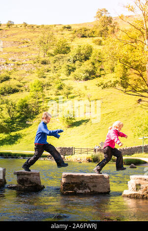 Einen kleinen Jungen und Mädchen hoffen, über die dovedale Trittsteine über einen Fluss, Bach im Peak District National Park, Derbyshire, Autismus springen Stockfoto