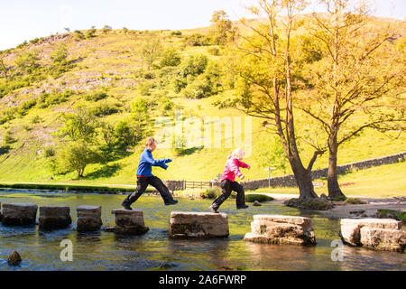 Einen kleinen Jungen und Mädchen hoffen, über die dovedale Trittsteine über einen Fluss, Bach im Peak District National Park, Derbyshire, Autismus springen Stockfoto