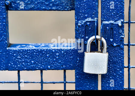 Ein blau metallic Zaun mit einem silbernen Edelstahl Vorhängeschloss, Sicherheit Tor getränkt mit Regen Stockfoto