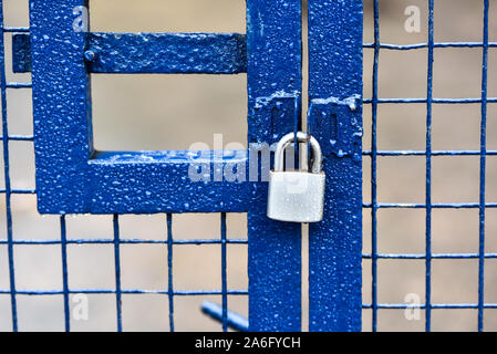 Ein blau metallic Zaun mit einem silbernen Edelstahl Vorhängeschloss, Sicherheit Tor getränkt mit Regen Stockfoto