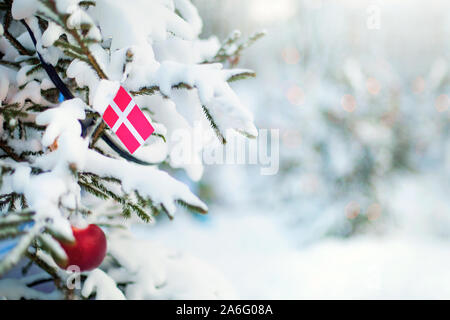 Weihnachten in Dänemark. Xmas Tree mit Schnee, Dekorationen und eine Flagge Dänemarks bedeckt. Verschneite Wald Hintergrund im Winter. Weihnachten Grußkarte. Stockfoto